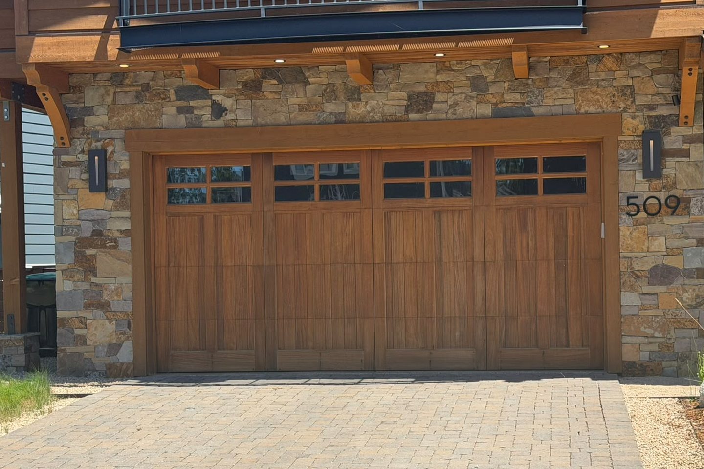 Custom wood-grain carriage garage door with window panels, framed in natural stone