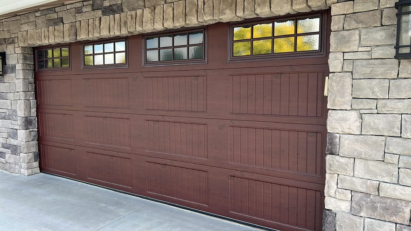 Mahogany wood-grain garage door with divided windows and stone surround